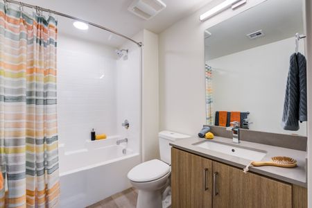 Model apartment bathroom with wood cabinets, quartz countertops, and white bathroom facilities