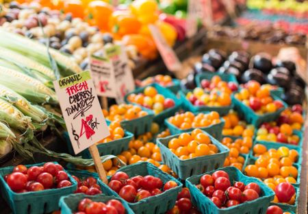 A farmers market with outdoor stalls and crates of fruits and vegetables including peppers, tomatoes, and corn.