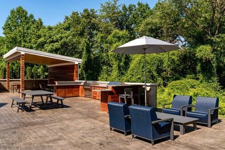 Outdoor lounge at our apartments for rent in Germantown, MD featuring an umbrella, benches, and grill station.