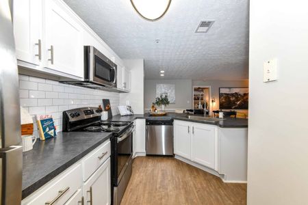 Renovated kitchen in an apartment for rent in Acworth, GA. White tile backsplash, dark gray countertops, white cupboards, stainless steel appliances and hardwood floor.