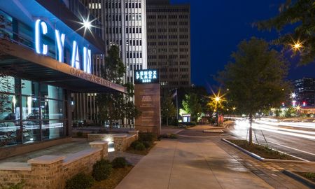 The exterior of the Cyan on Peachtree apartments at night in Atlanta, GA, featuring a sign that reads The entrance to our apartments for rent in Atlanta, featuring a view of Lenox Plaza and the city high rise buildings.
