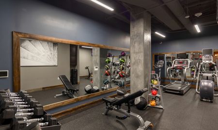 The gym at our apartments for rent in Washington DC, featuring weight balls, a bench press, and free weights.