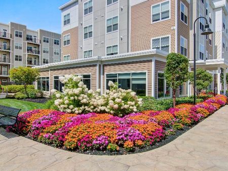 The grounds at our apartments in Wakefield, featuring a cobblestone path, colorful flowers, and a view of the apartments.