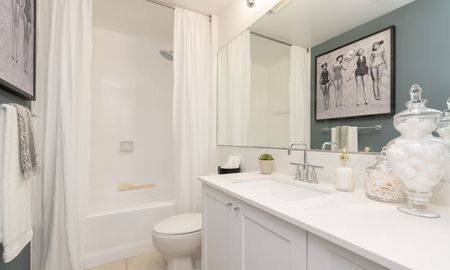 Model bathroom at our apartments in Pompano Beach, FL, featuring white counters, a large mirror, and shower/bath combo.