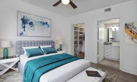 Model bedroom at our apartments in Pompano Beach, FL, featuring wood laminate floors and a view of the bathroom and closet.