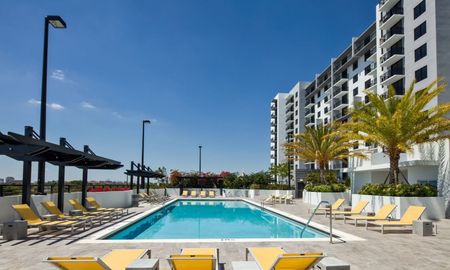 The pool area at our apartments in Miami, featuring yellow reclining chairs, a shade structure, and a sparkling blue pool.