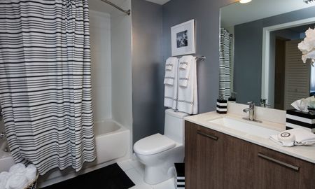 Model bathroom at our apartments in Miami, featuring wood laminate cupboards, white tile floors, and a shower / bath.