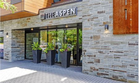 The exterior of The Aspen apartment community, featuring sliding glass doors and a stone masonry facade.