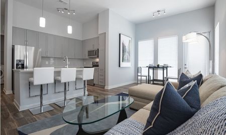 Model living room at our apartments for rent in Sandy Springs, featuring wood grain floor paneling and a view of the kitchen.