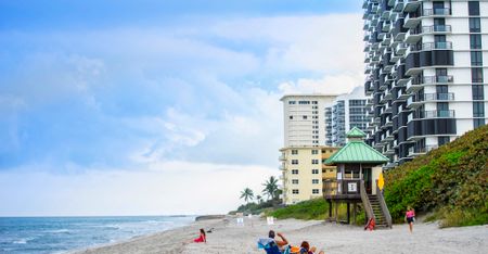 Photograph of the beach near our apartments in Boca Raton, featuring people sunbathing and a view of the apartment complex.