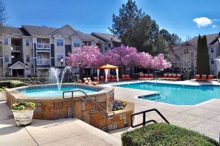 The pool area at our apartments for rent in Mooresville, NC, featuring beach chairs, flowering trees, and a fountain.