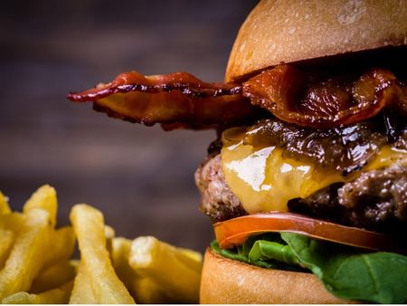 Stock photograph of a burger with bacon and fries. The burger is half visible and there is a grey background.