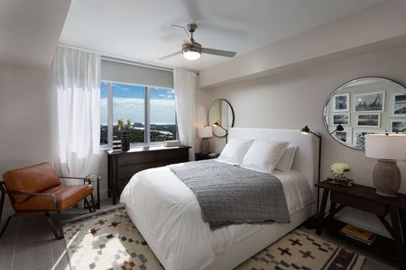 Model bedroom at our apartments in Fort Lauderdale, featuring white bedspread, a leather chair, and a large window.