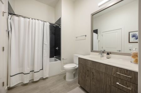 Model bathroom at our apartments in Watertown, featuring wood grain floor paneling and a bath / shower combination.