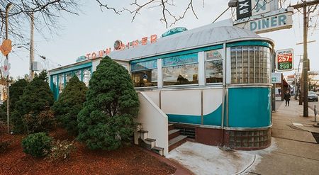 Photograph of a diner in a train car in the town of Watertown, featuring a view of the sidewalk and people walking.The Town Diner near our apartments for rent in Watertown, MA, featuring a old fashioned diner exterior.