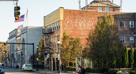 Photograph of the streets of Watertown, featuring a brick wall with a coca-cola logo painted on it, and storefronts.The streets of Watertown, MA, near our apartments outside of Boston, featuring brick buildings and cars on the street.