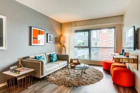 Model living room at our apartments in Cambridge, featuring bright orange chairs, a grey couch, and a flat screen TV.