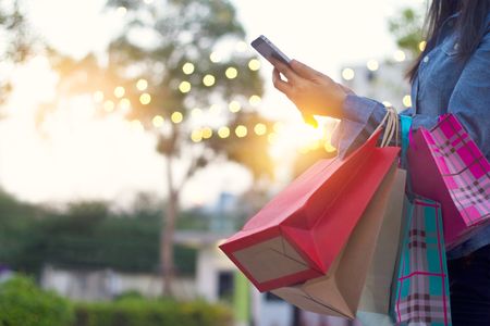 Lady reading mobile phone while holding multiple shopping bags.