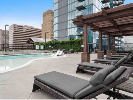 The pool area at our apartments in Atlanta, featuring reclining chairs, a shade structure, and a view of the apartments.