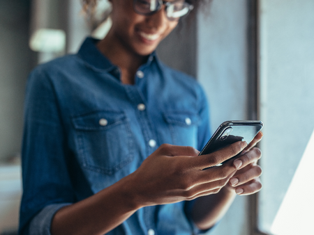 Stock photograph of someone smiling while looking at their phone. They are wearing blue denim and glasses.