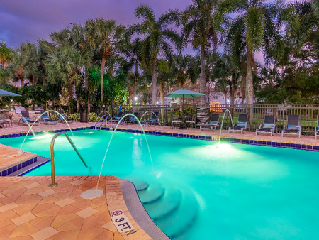 The pool area at our apartments in Palm Beach Gardens at night, featuring beach chairs, umbrellas, and palm trees.