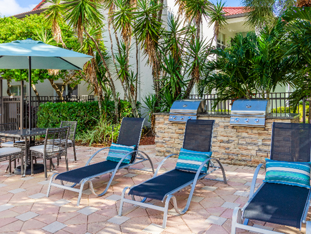 The pool area at our apartments in Palm Beach Gardens, featuring beach chairs, umbrellas, and grill stations.