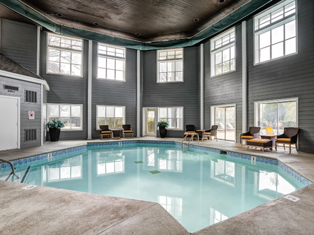 Indoor pool at our apartments in Nashville, TN, featuring cushioned chairs with small tables and a large octagonal pool.