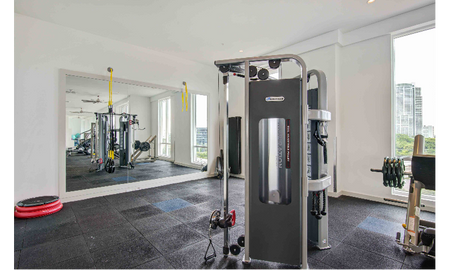 Fitness center at our apartments in Brickell, featuring assisted weight lifting machines, padded floors, and a mirrored wall.