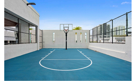 The basketball courts at our apartments in Brickell, featuring a blue clay court and a hoop with a glass backboard.