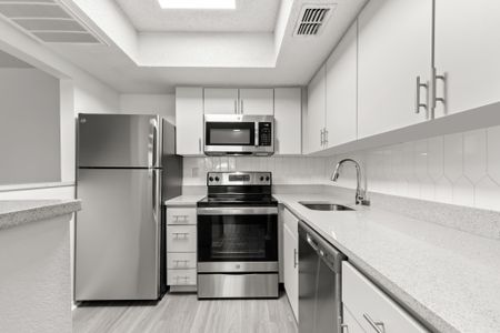 Model kitchen at our apartments in Clearwater, FL, featuring stainless steel appliances, grey counters, and white cubpboards.