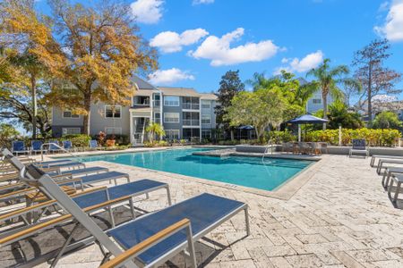 Outdoor pool with tiled flooring, seating, and surrounding trees.