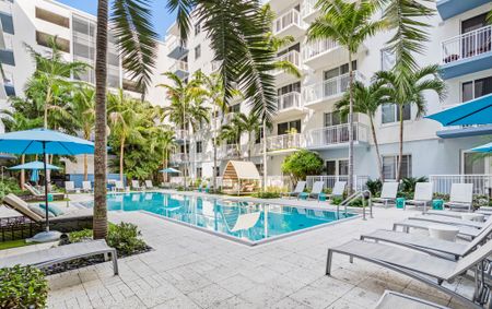 Pool area at our apartments in Boca Raton, featuring reclining chairs, umbrellas, palm trees, and a view of the City Walk Apartments.