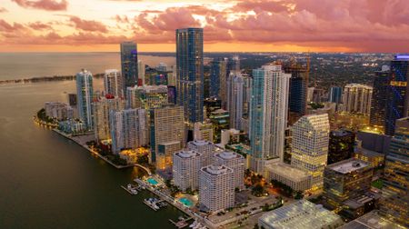 Aerial view of the city of Miami, FL at sunset, featuring a view of the ocean city high rise buildings