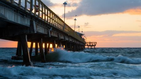 The pier near our apartments for rent in Pompano Beach, featuring waves crashing on the beach with a sunset.