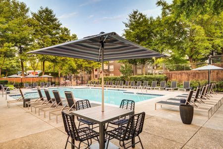 The pool area at our apartments for rent in Owings Mills, MD, featuring beach chairs, umbrellas, and trees.