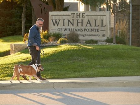 A man walking a dog in front of a large outdoor sign for the Winhall of Williams Point Apartments in Waukee, Iowa | The Winhall of Williams Pointe