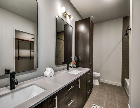 Bathroom with dual vanity, deep brown cabinets and upgraded lighting, and linen closet