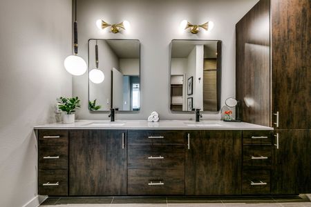 Bathroom with dual vanity, deep brown cabinets and upgraded lighting, and linen closet