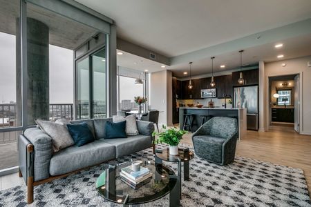 Furnished and decorated living area overlooking upscale kitchen with floor to ceiling windows and downtown views