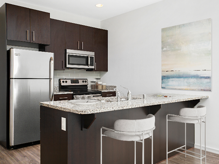 Three-Bedroom Apartments In Downtown Milwaukee, WI - The Moderne - Kitchen With Dark Brown Cabinets, Granite-Style Countertops, And Appliances.