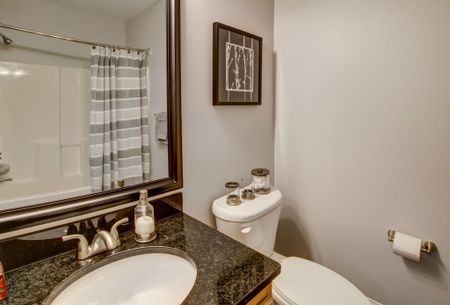 Bathroom vanity with framed mirror hung above. Toilet to the right. Tub/Shower can be seen in mirror reflection.