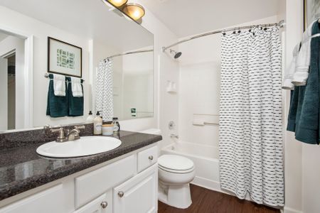Model bathroom with granite countertops, plank flooring and a bathtub shower combo