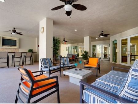 Covered sitting area with couches, chairs, outdoor bar, television, and ceiling fans