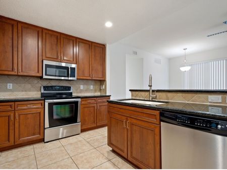 Kitchen with tile back splash, cabinets, sink, stainless steel oven, microwave, and dishwasher looking into living room