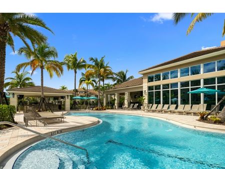 Pool surrounded by lounge chairs and palm trees in front of club house with floor to ceiling windows