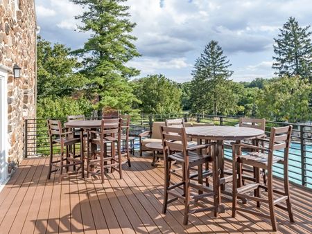 Wooden table and chairs outside on clubhouse deck overlooking trees and sky.