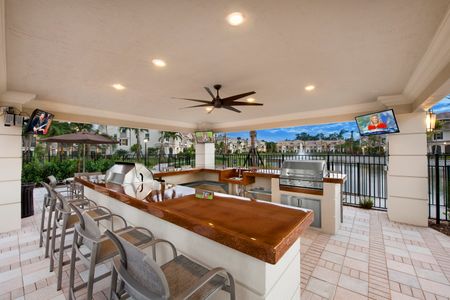 Covered open air outdoor grilling area with 2 stainless steel grills, ceiling fans, ample bar seating and fountain view