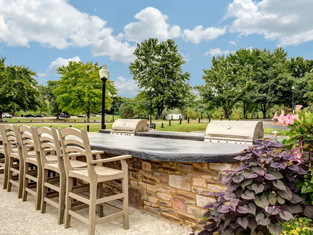 Bellevue West Apartments Outdoor Community Kitchen with Multiple BBQ Grills, Large Table, and Lush Greenery Views