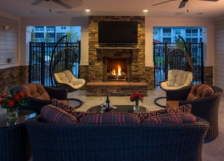 Evening view of seating area and outdoor television under pool cabana with fireplace on
