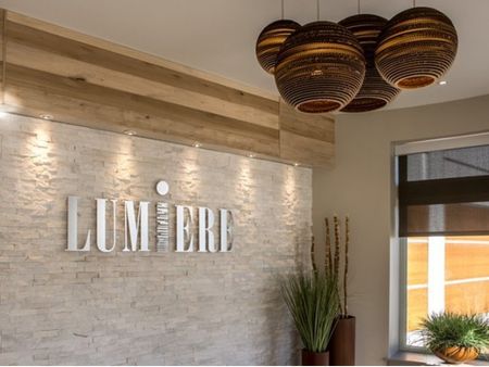 White brick lobby wall with Lumiere logo sign and four brown, circular lights hung from ceiling